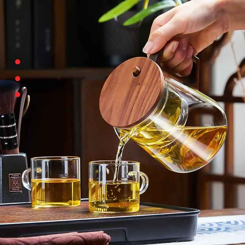 Elegant heat-resistant glass teapot with water separation design, pouring tea into cups.